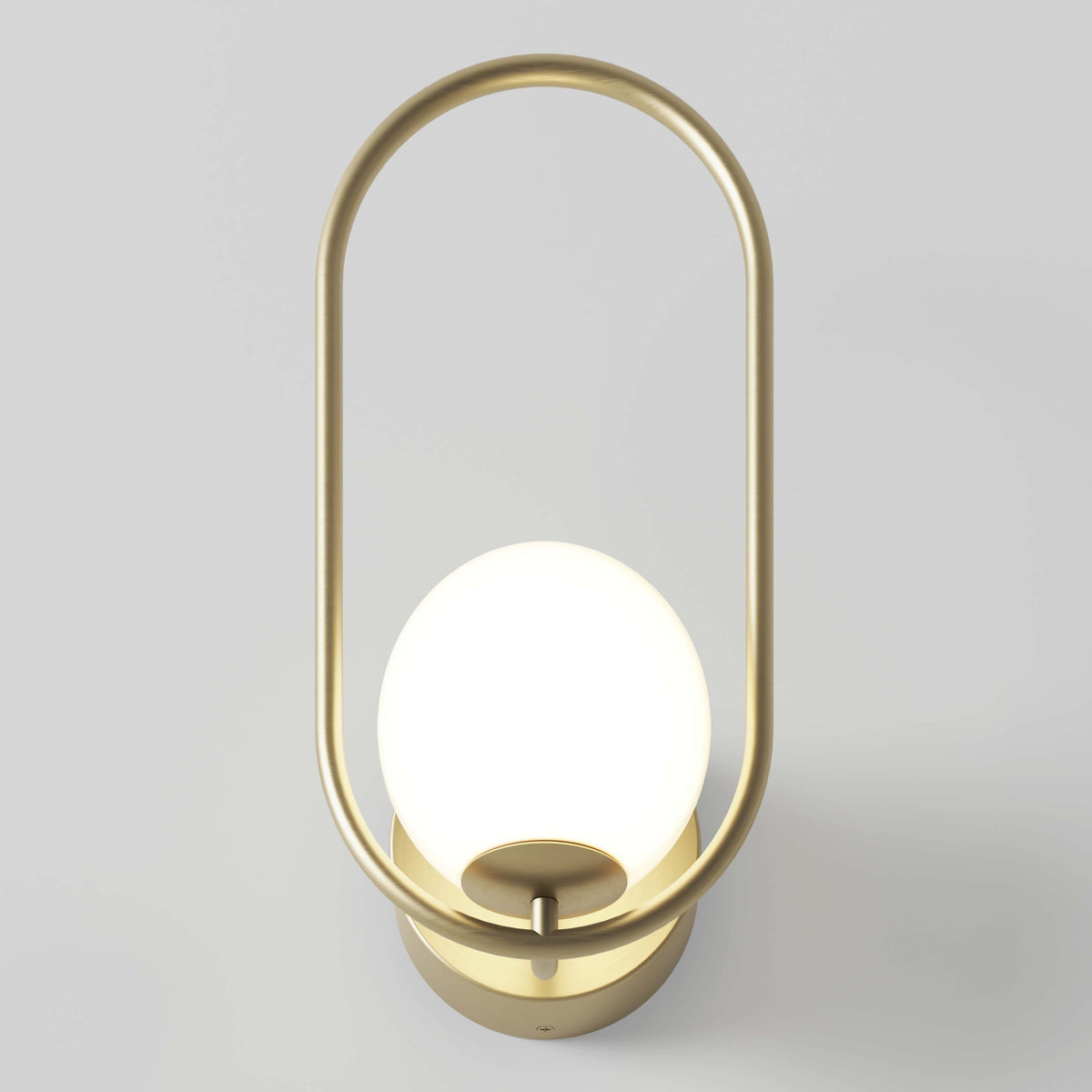 A modern wall sconce with a brass oval frame and a glowing white glass globe as the light source, mounted on a light-colored wall.