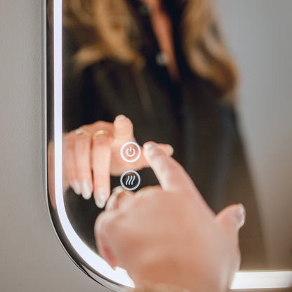 Someone adjusts the colour on the Artika Royce 24″x32″ Dimmable Anti-Fog LED Mirror, seeing their reflection in its lit glass.