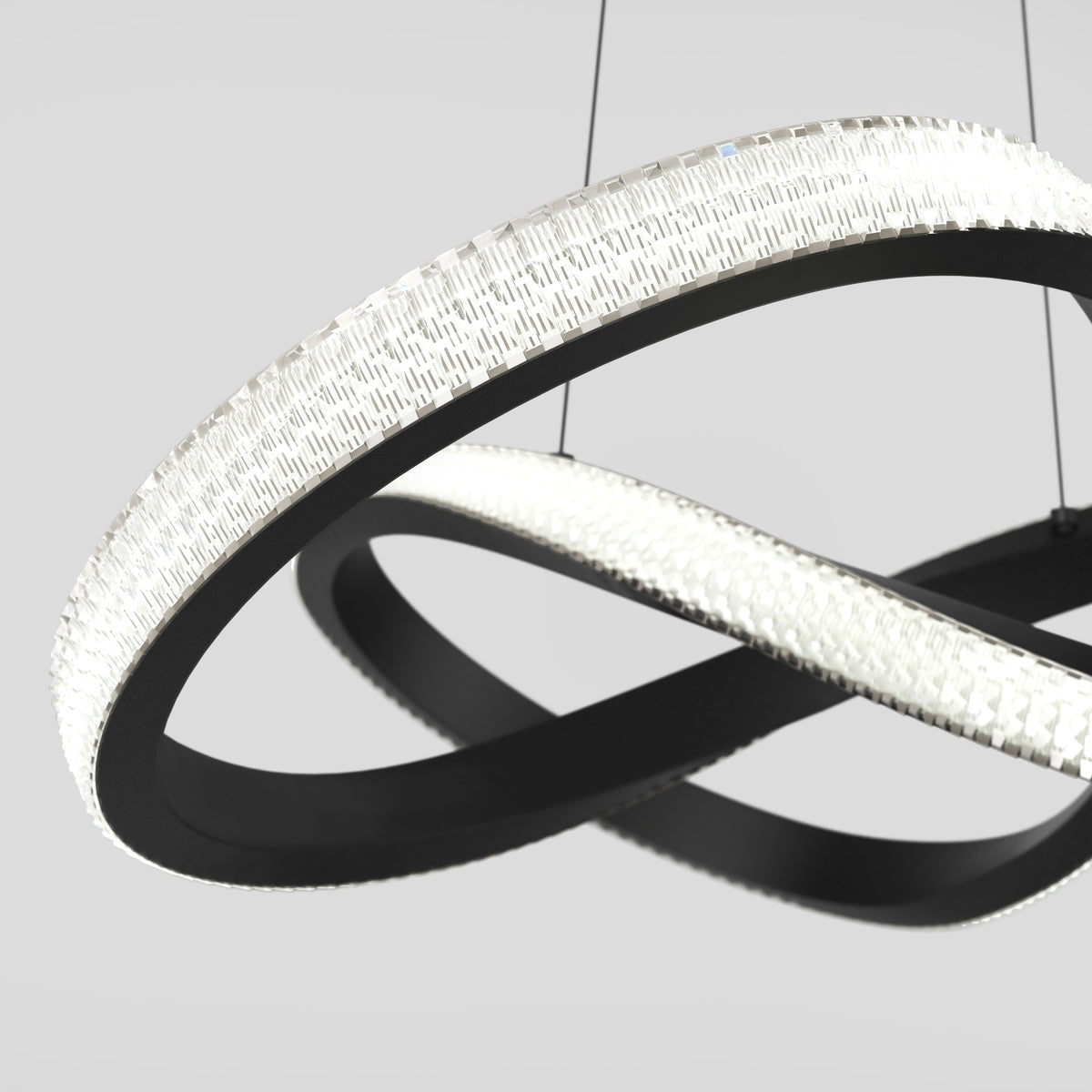 A modern, sculptural LED chandelier with interlocking black rings featuring textured, illuminated surfaces, suspended by thin wires against a light gray background.