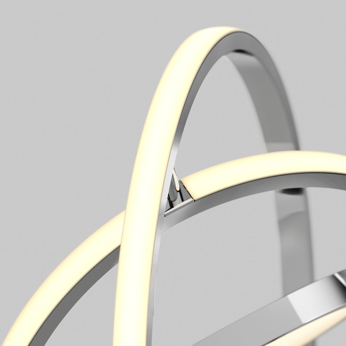 Close-up of a modern light fixture with intersecting metallic rings and integrated LED strips emitting a soft, warm white glow, set against a plain gray background.