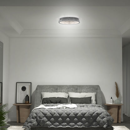 A modern bedroom with a gray upholstered bed, checkered bedding, two wooden nightstands with decor, framed artwork, and an Artika Glitter LED flush mount ceiling light. The walls and ceiling are white.
