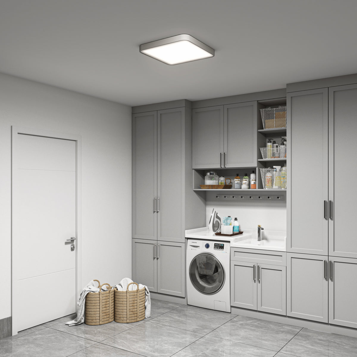 A modern laundry room with gray cabinets, a front-loading washing machine, a built-in sink, shelves with cleaning supplies, and two wicker laundry baskets filled with towels on a tiled floor.