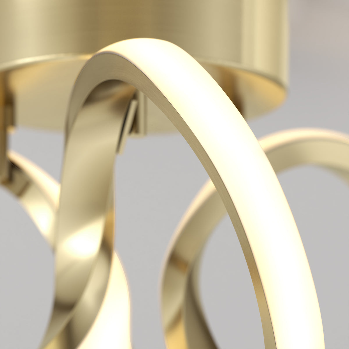 Close-up of a modern, gold-colored metallic light fixture with smooth, curved arms and a shiny surface, set against a neutral background.