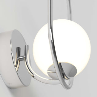 The Artika Bloom LED Sconce 3 CCT features a round white glass globe held by curved chrome arms on a circular chrome base, giving any light gray wall a modern touch.