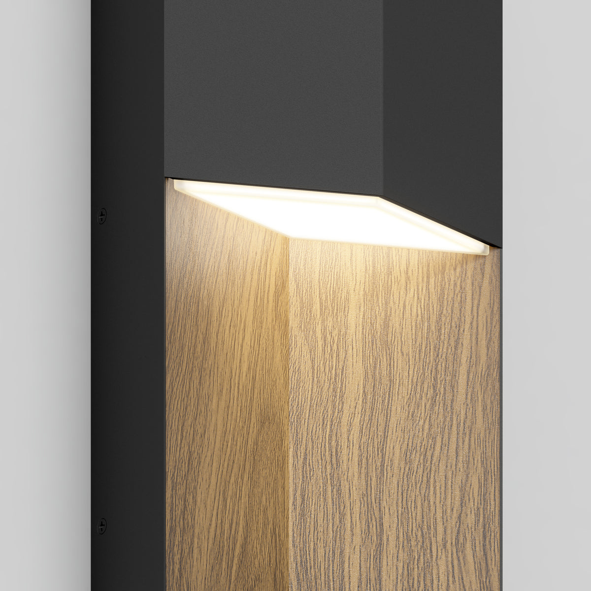 A modern wall light fixture with a black exterior and inner wooden panel, mounted on a white wall, emits a warm white glow downward.