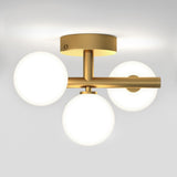 A modern ceiling light fixture with a gold metallic base and three round, frosted white glass globes evenly spaced around it, mounted on a white ceiling.