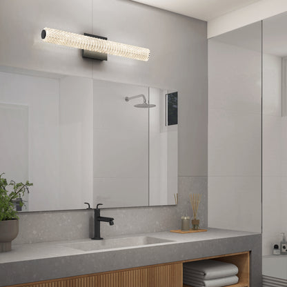 Modern bathroom with a large mirror, an Artika Exalto LED bathroom vanity light above it, black faucet, plant, toiletries on the gray countertop, and neatly folded towels on a wooden shelf below.