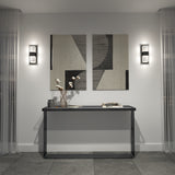 A modern entryway with a slim black console table holding a vase with cotton branches, books, and a small tray, set against a light wall with two abstract art pieces and two wall sconces, flanked by sheer curtains.