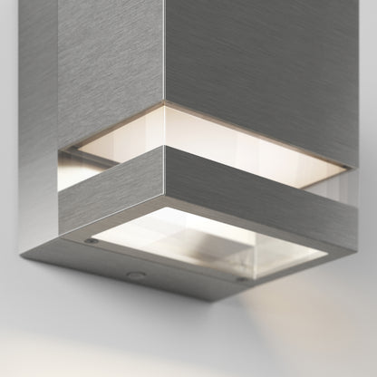 Close-up of the Artika Valor Square LED indoor-outdoor wall light, featuring a brushed metal finish and frosted glass panel, mounted on a white wall and casting soft, diffused illumination downward.