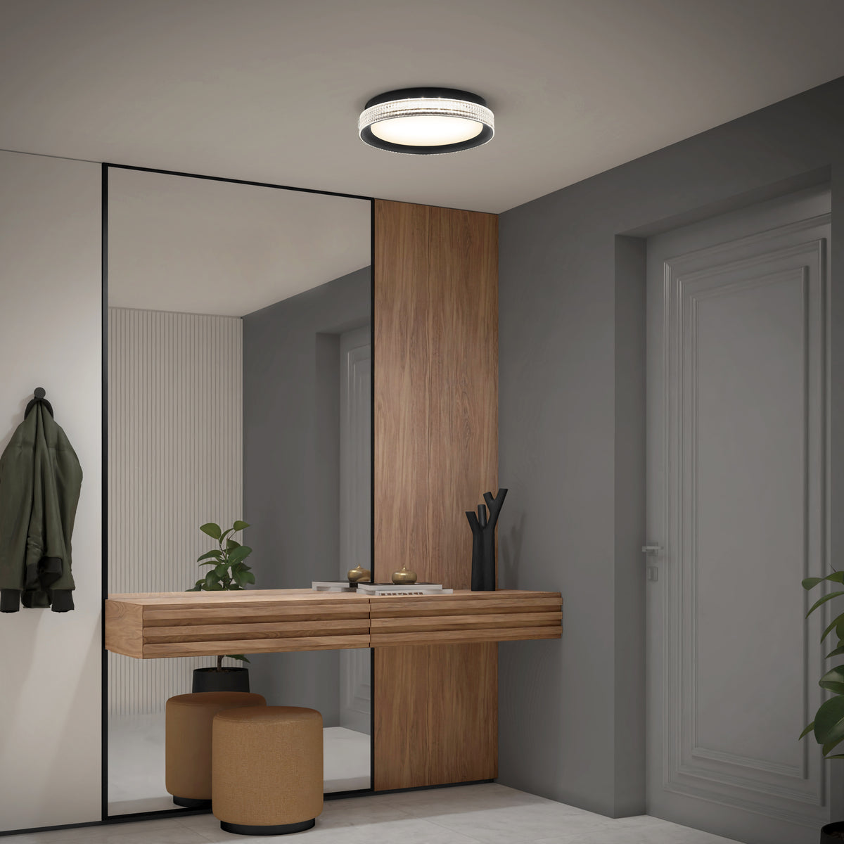 A modern hallway with a large mirror, wooden floating console, two round tan stools, green coat on a hook, potted plant, decorative items, gray door, and a circular ceiling light.