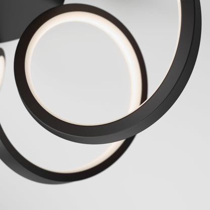 Close-up of the Artika-CAN-dev Swirl Ribbon LED pendant light, showcasing two intertwined black rings with integrated LEDs against a plain light gray background for a sleek, modern look.