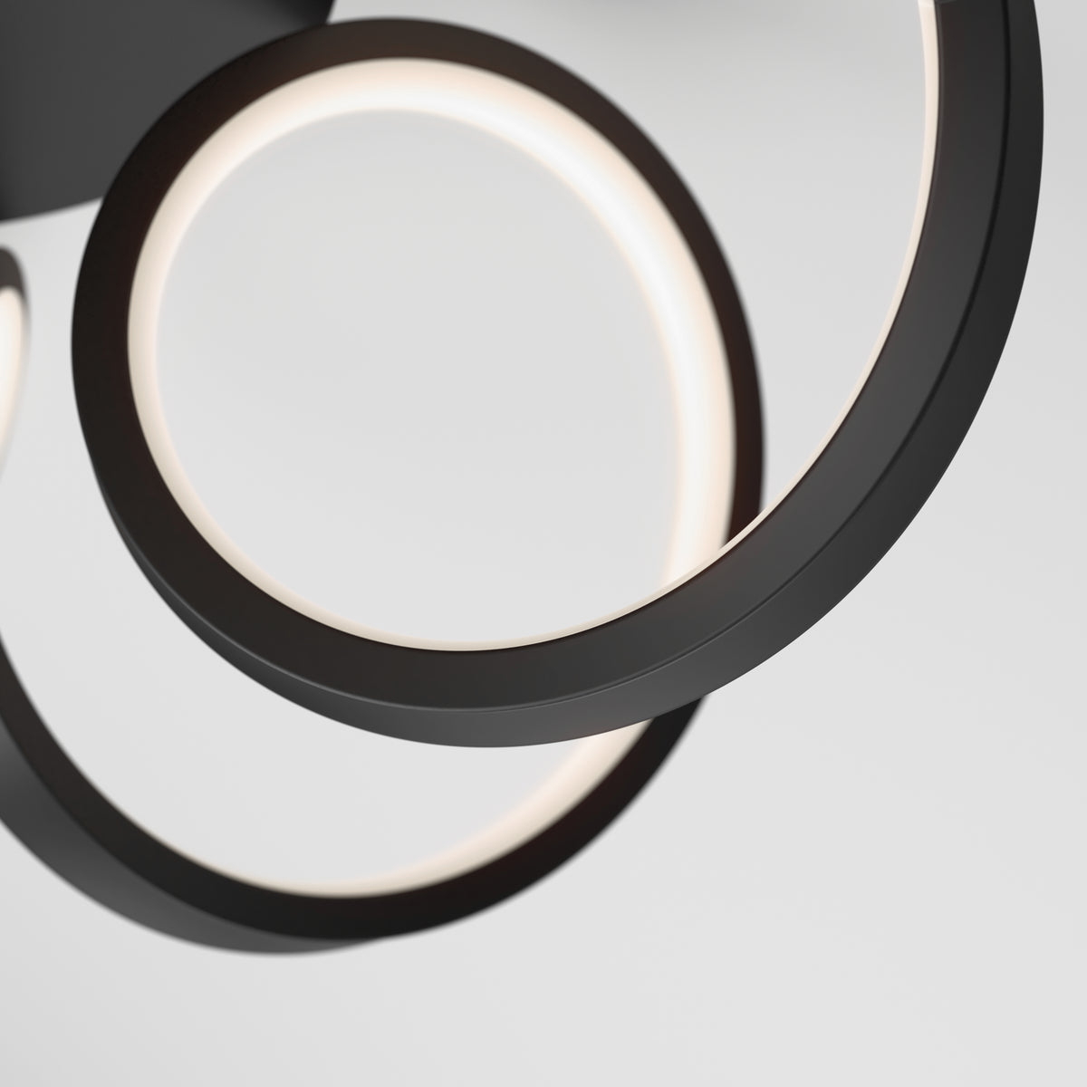 Close-up view of a modern, circular LED ceiling light fixture with black frames, featuring two overlapping illuminated rings against a plain white background.