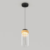 A modern pendant ceiling light with a black mount, a thin black cord, a wooden accent, and a clear cylindrical glass shade, hanging against a plain light gray background.