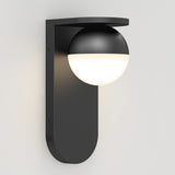 A modern black wall sconce with a matte finish, featuring a round globe-shaped light partially covered by a curved top shade, mounted on a flat vertical base against a white wall.