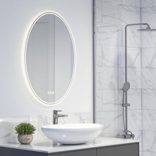 Modern bathroom with an Artika Corby 22 in. x 28 in. LED mirror (3 CCT, defogger), white oval vessel sink, silver faucet, small potted plant, and a shower with gray tiles and a handheld showerhead.