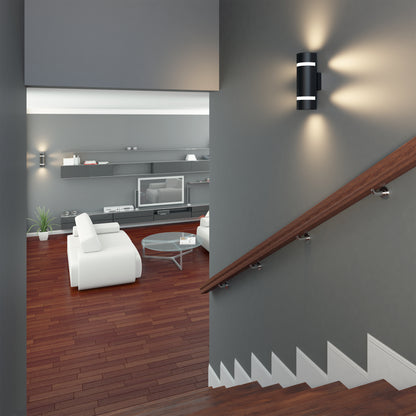 A modern living room with dark wood floors, white sofas, a round glass coffee table, built-in shelves with a TV, seen from a staircase with a wooden handrail and an Artika D4 indoor-outdoor wall light.