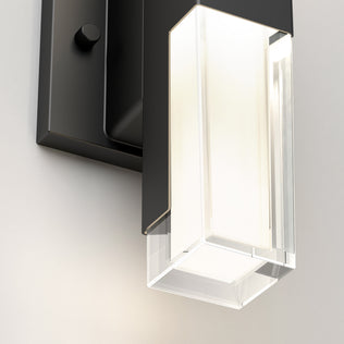 Close-up of the Artika Gemini indoor-outdoor LED wall light, featuring a black rectangular base and clear glass shade, emitting a soft, warm white glow.