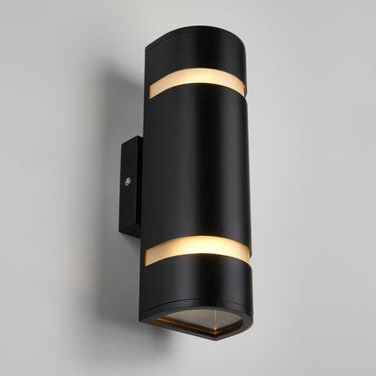 The Artika D4 indoor-outdoor wall light is a modern black cylindrical sconce with dual horizontal bands, casting up and down lighting when mounted on a light gray wall.