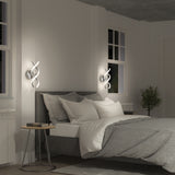 A modern bedroom with a gray upholstered bed, white and gray bedding, two small round bedside tables, unique spiral wall lights, a window, potted plant, and minimalist decor.