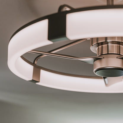 A close-up view of a modern ceiling fan with integrated LED lighting, featuring a circular light ring and sleek metallic blades, mounted on a light-colored ceiling.