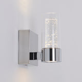 A modern wall sconce with a square chrome base and a cylindrical glass shade containing decorative bubbles, mounted on a white wall and illuminated.
