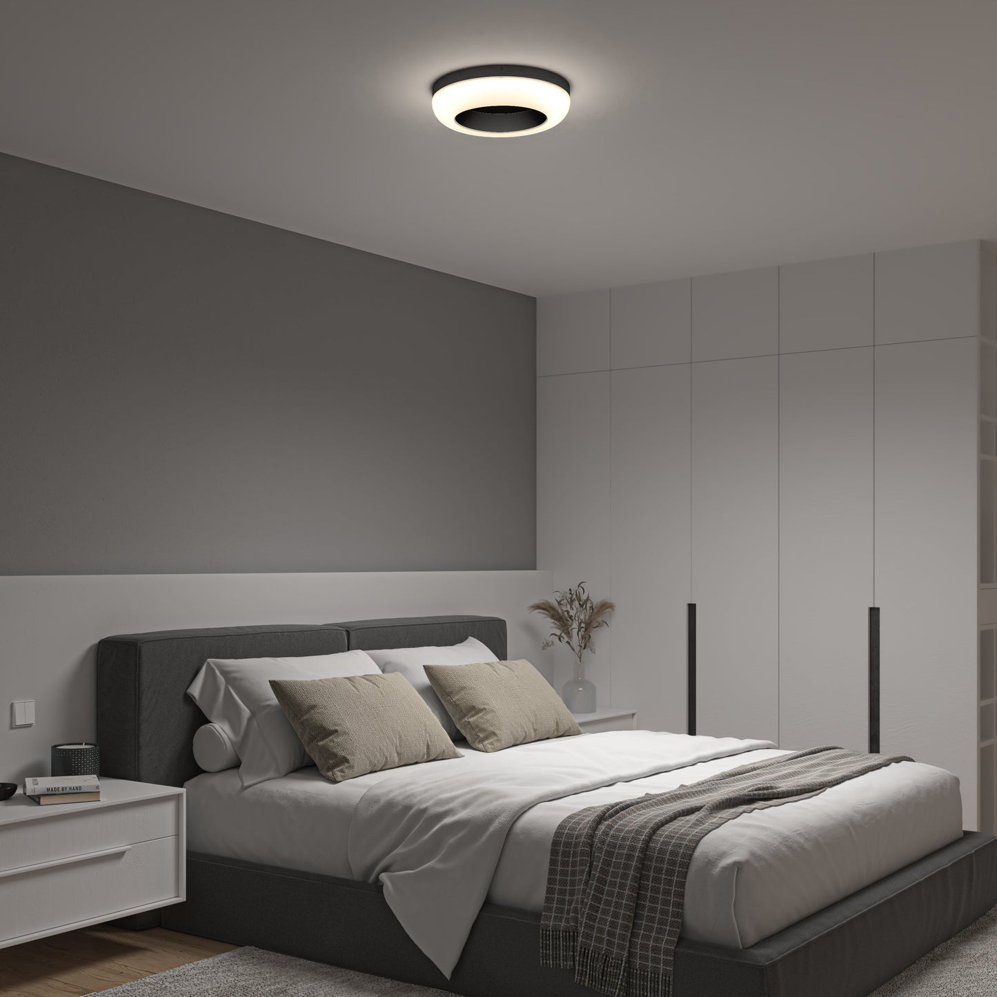 A modern bedroom features a gray accent wall, white closet doors, a tidy bed with gray and beige pillows, a bedside table with a vase, and is illuminated by the Artika-CAN-dev Louka 15 in. modern LED flush mount light 5 CCT with adjustable brightness.