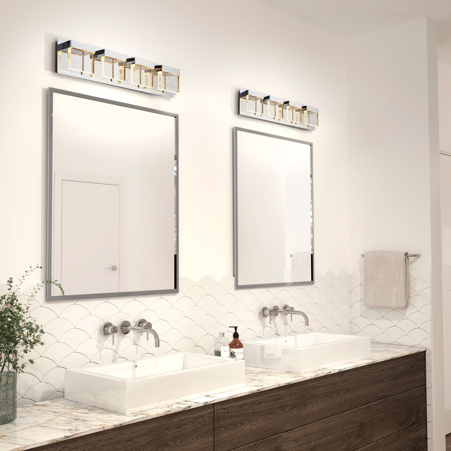 Modern bathroom with two rectangular mirrors above double sinks, wall-mounted faucets, marble countertop, and greenery. Above each mirror is an Artika Bubble Cube 4-light LED vanity light. A towel is hung on the wall.