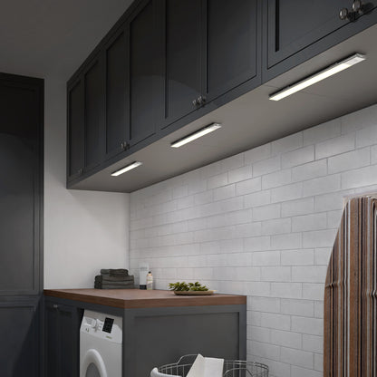 Laundry room features dark cabinets, white subway tile backsplash, wooden countertop, washer, stacked towels, wire laundry basket, ironing board; Artika Outline under cabinet LED light 3CCT is turned on.