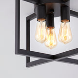 Close-up of a modern ceiling light fixture with three exposed Edison bulbs, surrounded by a black geometric metal frame against a white ceiling.
