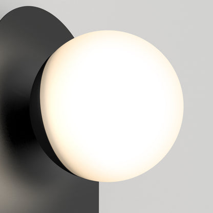 The Artika Bloomfield LED modern mid-century wall sconce 5 CCT features a matte black base and a large, round, frosted white glass bulb that provides soft, warm light against a light gray background.