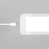 A white USB-C cable is positioned next to the corner of a rectangular, white-lit LED panel against a light gray background.