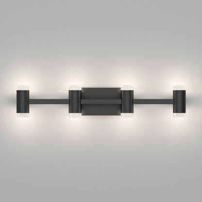 The Artika Mist modern LED bathroom vanity light 5 CCT features a matte black finish with four evenly spaced cylindrical lights and frosted ends, emitting a soft glow against a smooth gray wall.