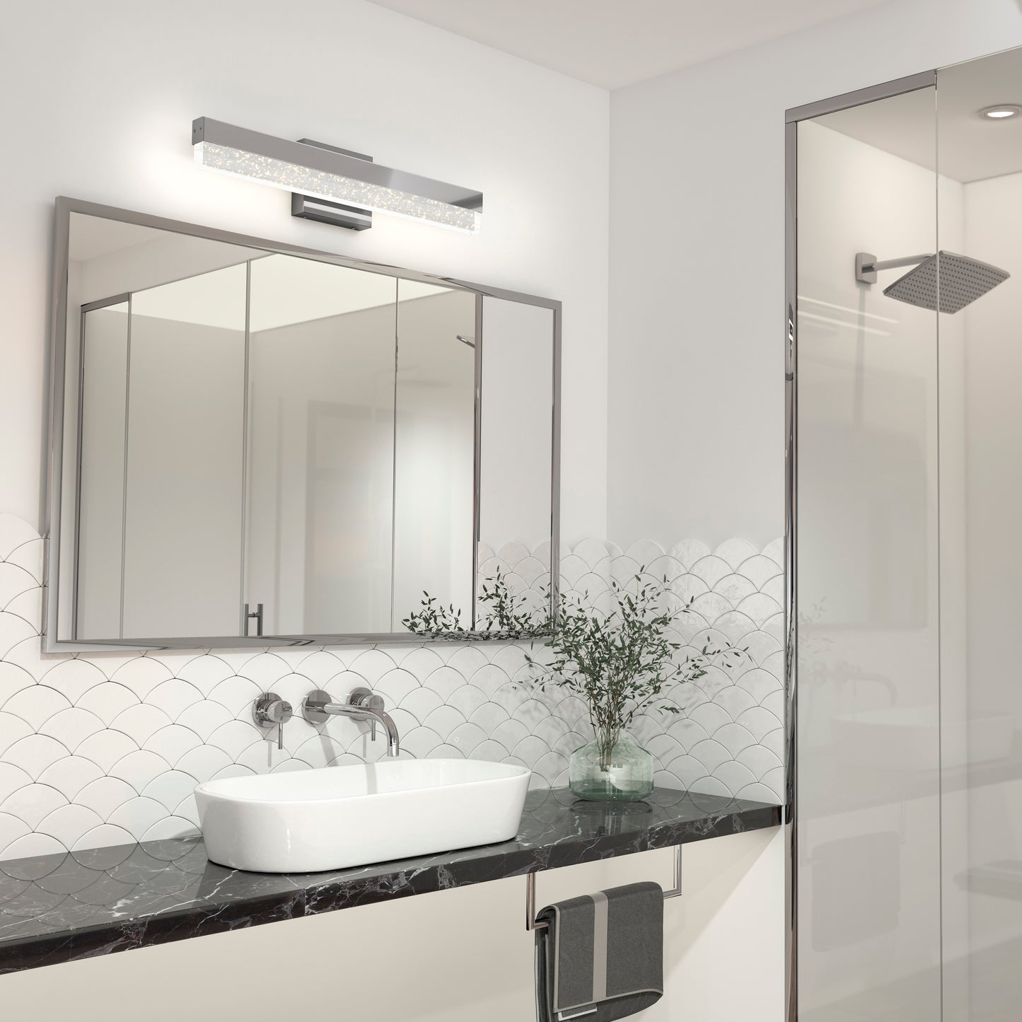 Modern bathroom featuring the Artika Essence Bubble Bar LED vanity light, a black marble countertop, white vessel sink, large mirror, wall-mounted faucet, towel rack, glass shower enclosure, and a decorative plant in a vase.