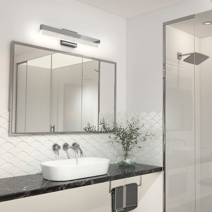 Modern bathroom featuring the Artika Essence Bubble Bar LED vanity light, a black marble countertop, white vessel sink, large mirror, wall-mounted faucet, towel rack, glass shower enclosure, and a decorative plant in a vase.