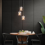 A modern dining area with a round wooden table set for four, black chairs, three pendant lights above, and a black textured wall in the background. A green potted plant is on the right side of the scene.