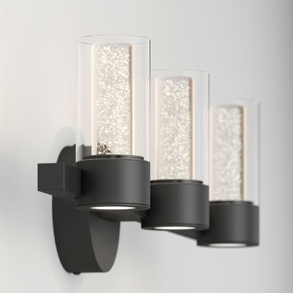 The Artika Novello modern LED bathroom vanity light features three bubble-filled cylindrical glass shades on a matte black base, wall-mounted against white.