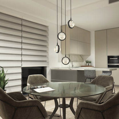 A modern kitchen and dining area with a round glass table, four cushioned chairs, Artikas Avalon 4-light LED pendant, beige cabinets, a built-in oven, a plant, and striped window blinds.