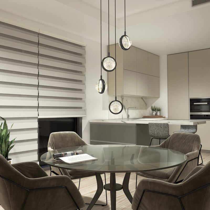 A modern kitchen and dining area with a round glass table, four cushioned chairs, Artikas Avalon 4-light LED pendant, beige cabinets, a built-in oven, a plant, and striped window blinds.