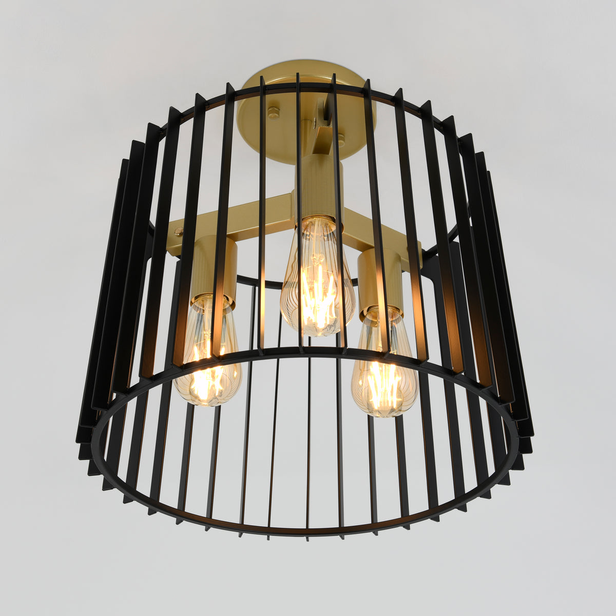 A modern ceiling light fixture with three exposed bulbs, enclosed in a cylindrical black metal cage with vertical bars and a gold-toned central structure, against a plain white background.
