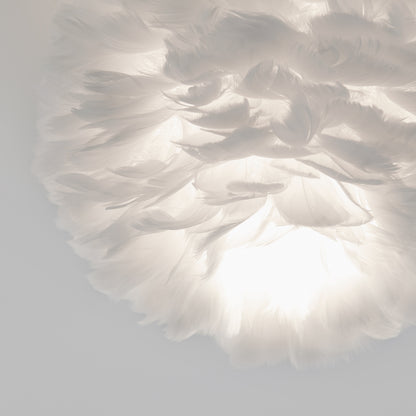 The Artika Plume LED flush mount light features a soft, white feather-inspired shade that glows warmly, creating an airy ambiance against a pale background.
