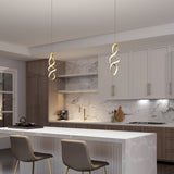 Modern kitchen with marble countertops and backsplash, two beige bar stools at a white island, gold spiral pendant lights, and wooden cabinets with gold hardware. Warm lighting creates a cozy, elegant atmosphere.