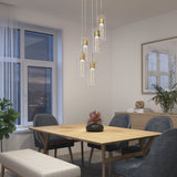A modern dining room with a wooden table, gray chairs, a bench, hanging pendant lights, a potted plant, a sideboard with decor, and a large window with sheer curtains showing an evening sky.