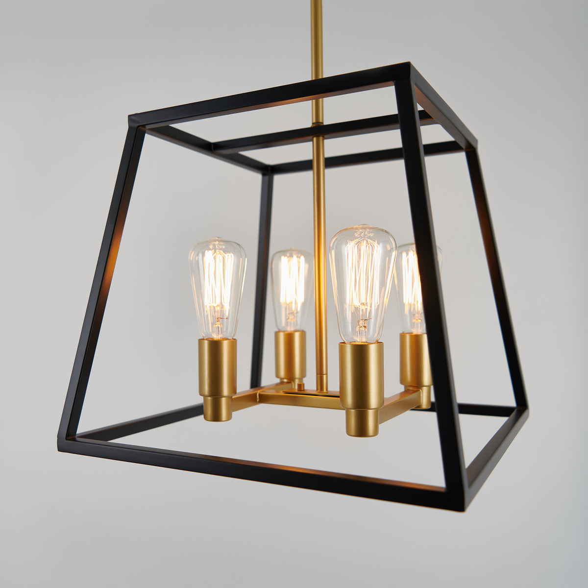 Modern pendant light fixture with four exposed Edison bulbs, gold sockets, and a geometric black metal frame, hanging against a plain light gray background.