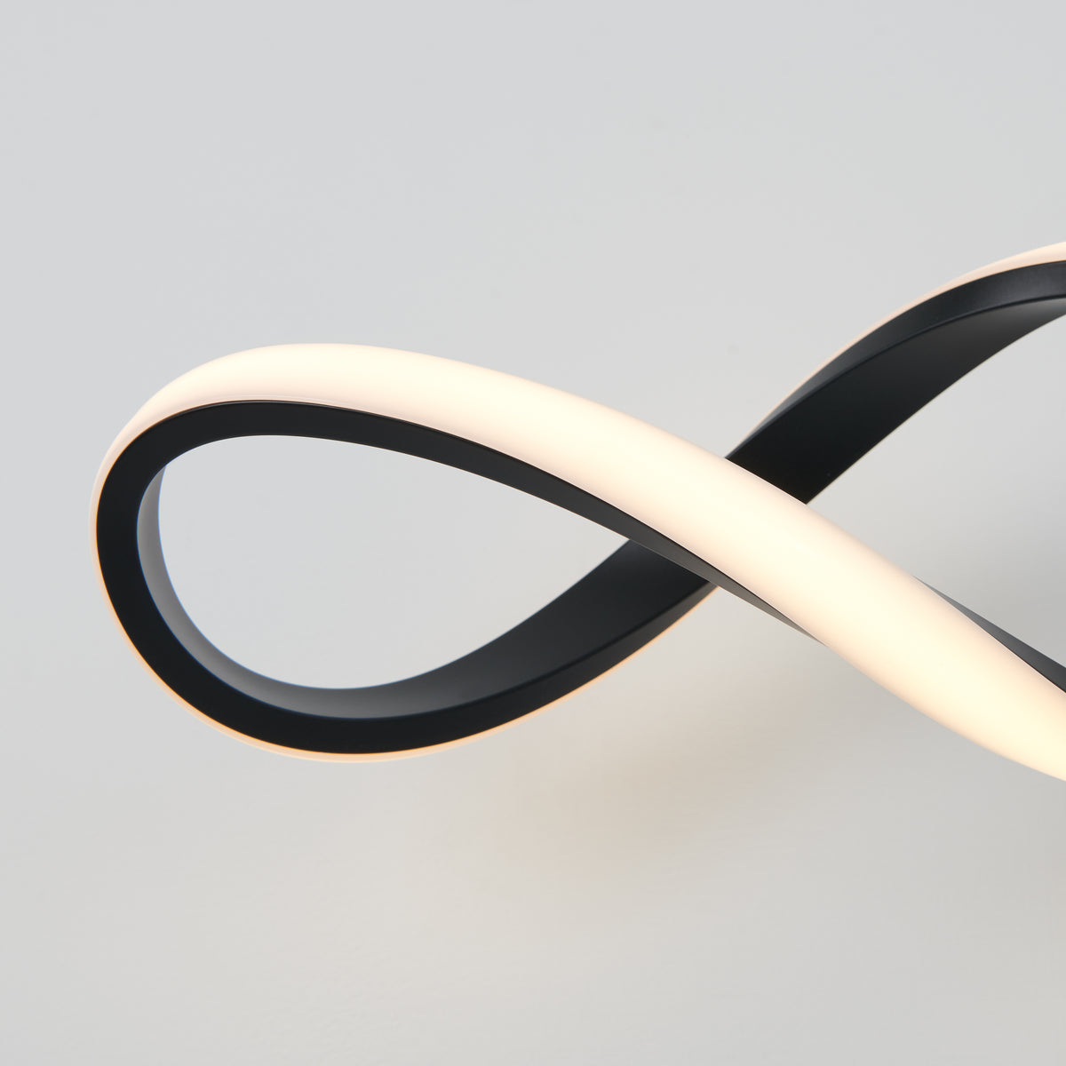 A modern, black and white LED light fixture forms a smooth, continuous infinity loop shape against a plain, light grey background.