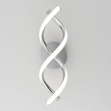 A modern wall sconce with two intertwined LED light tubes, one metallic and one glowing white, mounted on a round silver base against a plain light gray background.