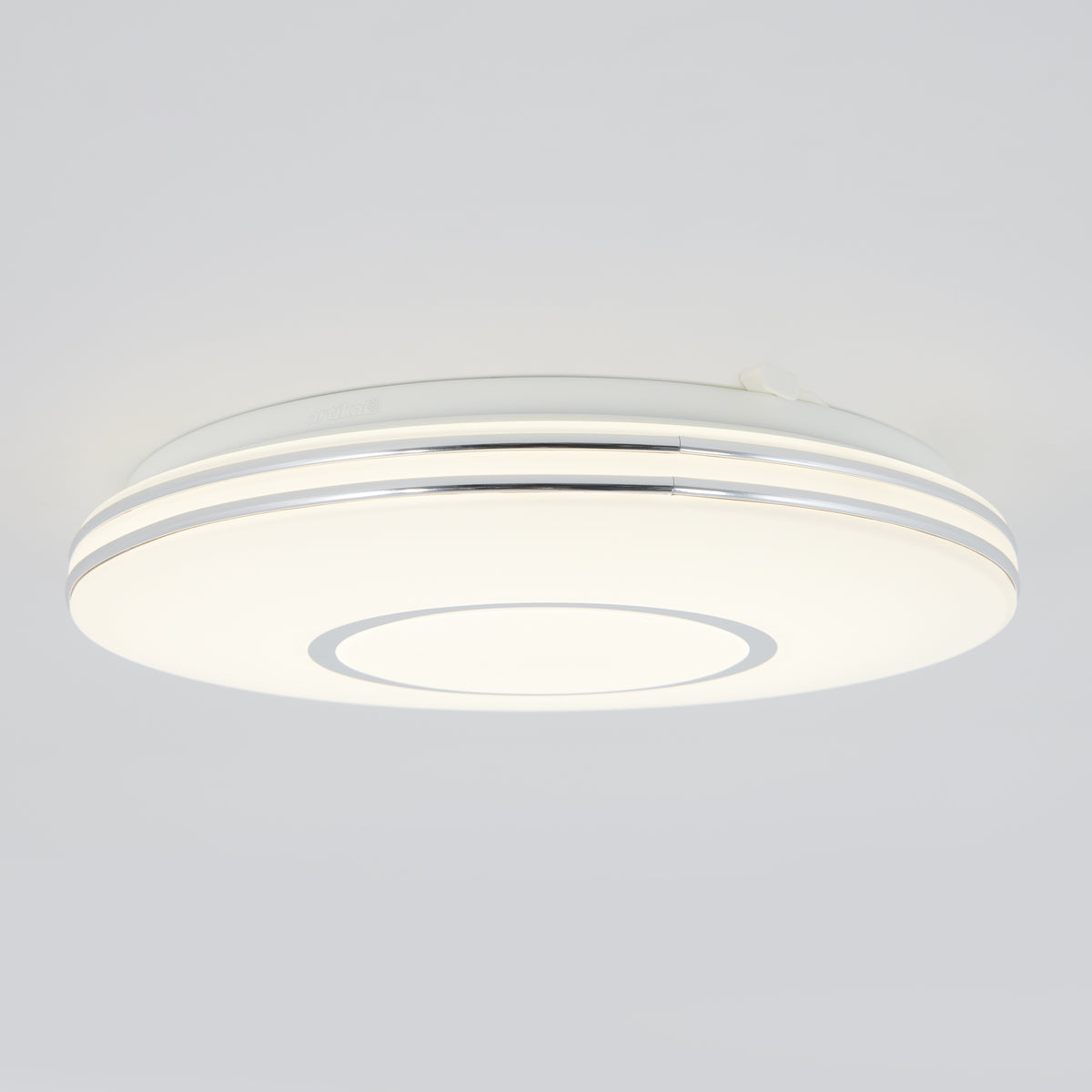 A modern, round ceiling light fixture with a sleek white design and subtle silver accents, mounted on a plain light-colored ceiling.