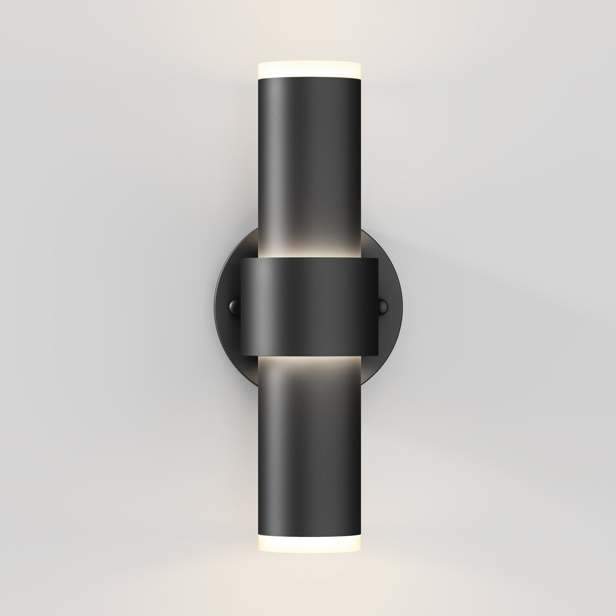 A modern black wall sconce light fixture with a cylindrical design, mounted on a round base, emitting light from both the top and bottom ends against a white wall.