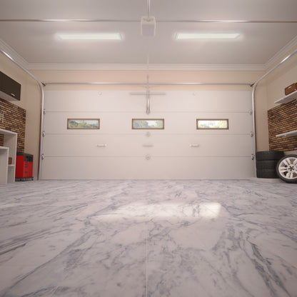 Wide-angle view of a clean, empty garage with marble flooring, white walls, closed double garage door with three small windows, shelves on the sides, a stack of tires on the right, and an Artika Sunray ultra thin LED light panel 3 CCT overhead.