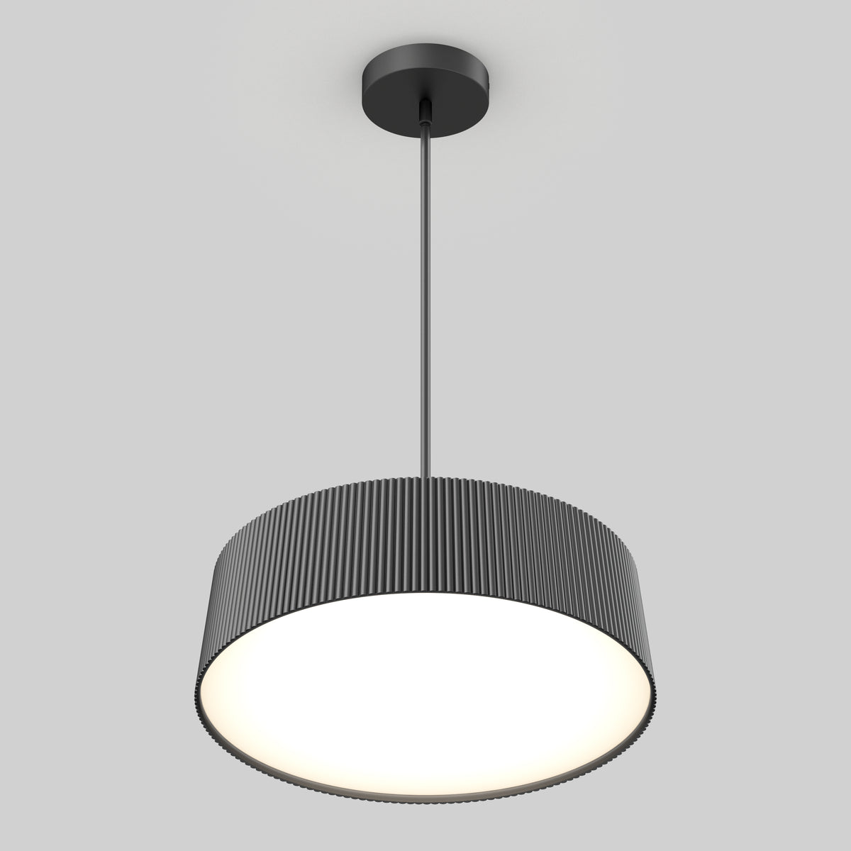 A modern pendant ceiling light with a round, ribbed, black lampshade hanging from a black rod, glowing brightly against a plain light gray background.
