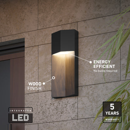 The Artika Howel modern LED indoor-outdoor wall light 5 CCT features a wood finish, integrated energy-efficient LEDs (no bulbs needed), a 5-year warranty badge in the bottom right, and some green plant leaves are visible.
